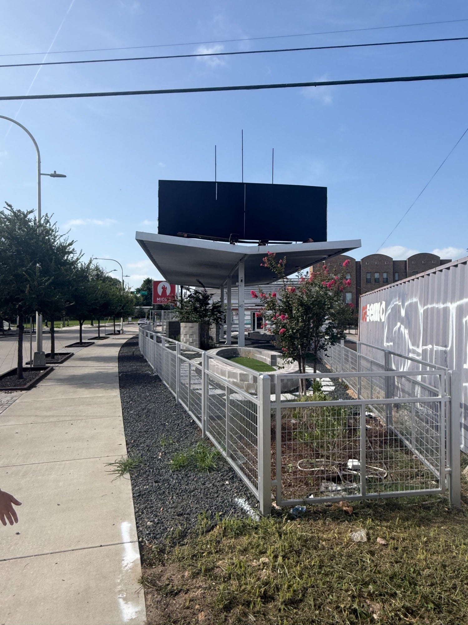 Sign tower and folded canopy seen from the sidewalk, courtyard fenced off